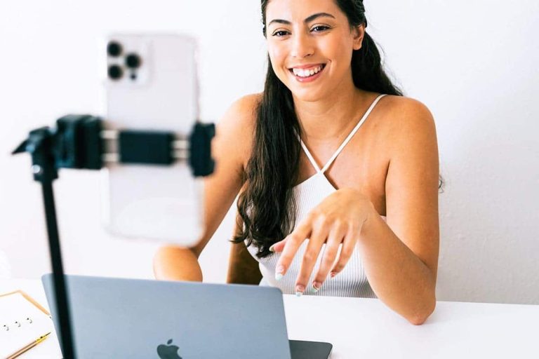 Latina small business owner recording a video with her phone and laptop, explaining why do you need a website for your business.