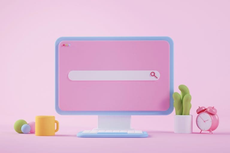 A pastel-colored computer monitor on a pink background displaying a minimalist search bar, symbolizing SEO and search engine visibility for small businesses. Surrounding the monitor are a yellow coffee mug, colorful decorative balls, a green plant, and a pink alarm clock, adding a playful and modern touch.