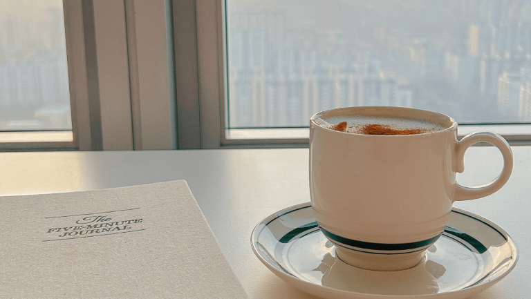 A calming moment with a cinnamon coffee and The Five-Minute Journal by the window, symbolizing the kind of rest and reflection your website can help you reclaim when it starts doing the work for you.