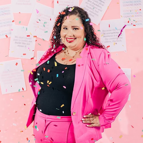 Confident Latina entrepreneur in a hot pink suit smiling amid falling confetti. Business copy and pink-toned backdrop reinforce a celebratory, strategy-driven vibe.