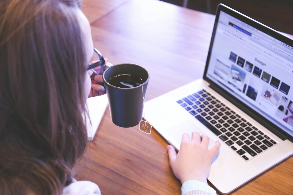 A person holds a mug of tea while looking at a laptop displaying a design inspiration or website layout page. The image conveys a quiet review and planning moment often involved in evaluating or refining website design and content.