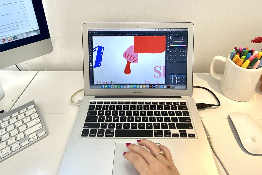 A person works on a laptop displaying a design file while sitting at a clean white desk with creative tools nearby. The image represents active design work involved in modernizing an outdated website.