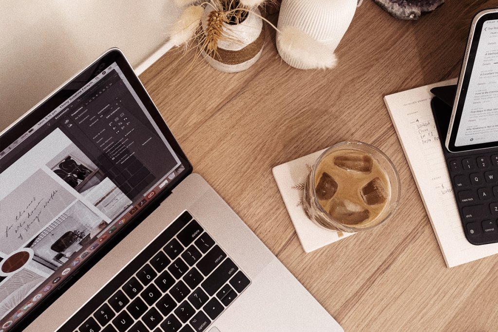 A laptop sits open on a wooden desk showing a content and design layout next to an iced coffee and notebook. The calm workspace reflects behind the scenes work often needed to update an outdated website with better visuals and structure.